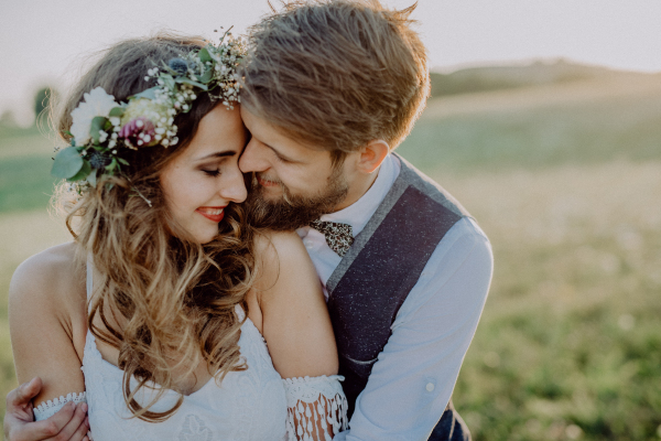 Beautiful young bride and groom outside in green nature at romantic sunset.