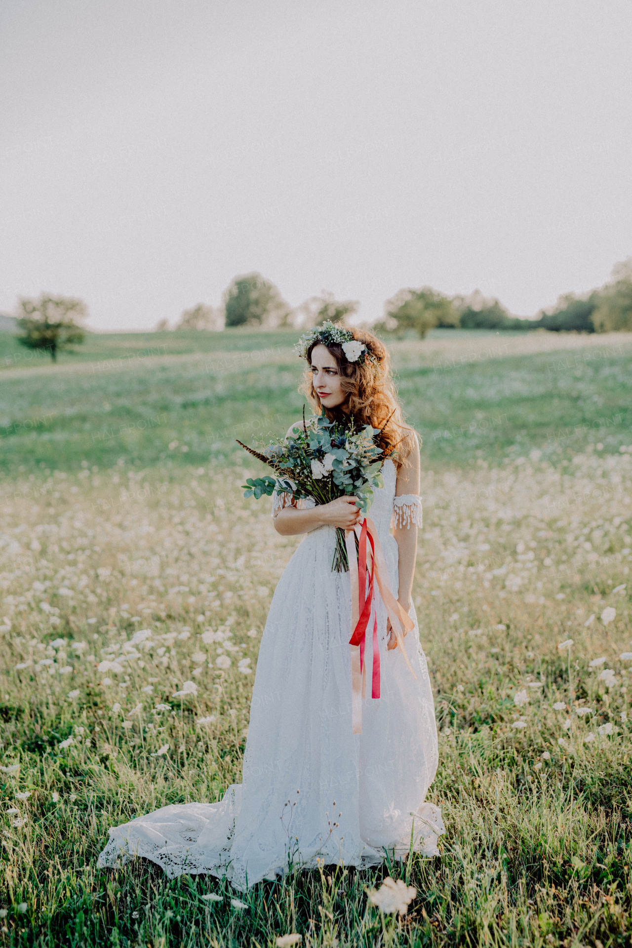 Beautiful young bride with flower wreath outside in green nature at sunset.