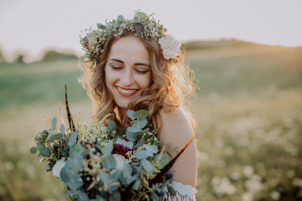 Beautiful young bride with flower wreath outside in green nature at sunset.