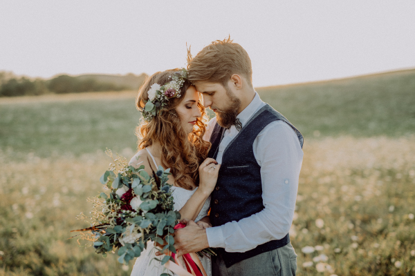 Beautiful young bride and groom hugging outside in green nature at romantic sunset.