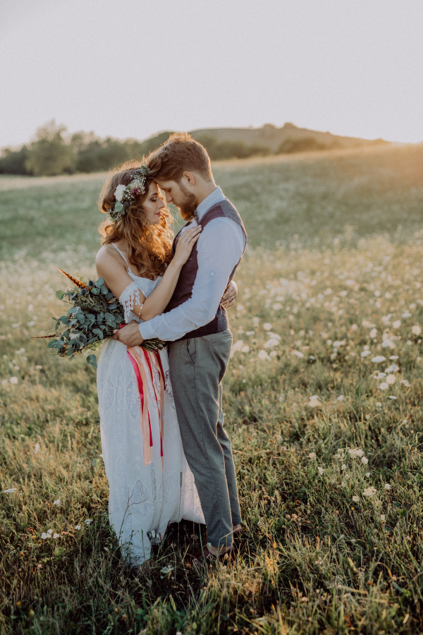 Young bride and groom outside in green nature at romantic sunset, hugging.