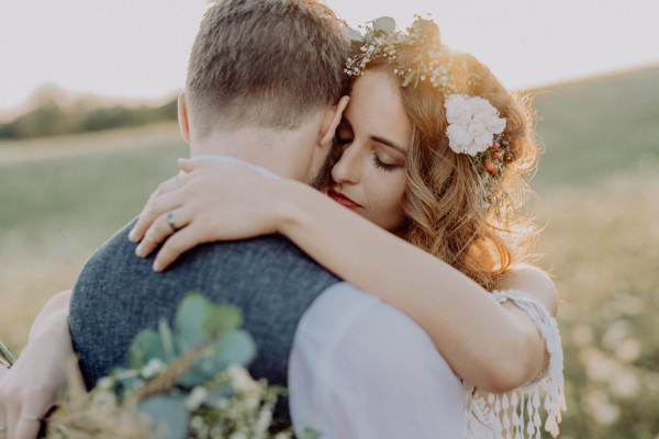 Young bride and groom outside in green nature at romantic sunset, hugging.