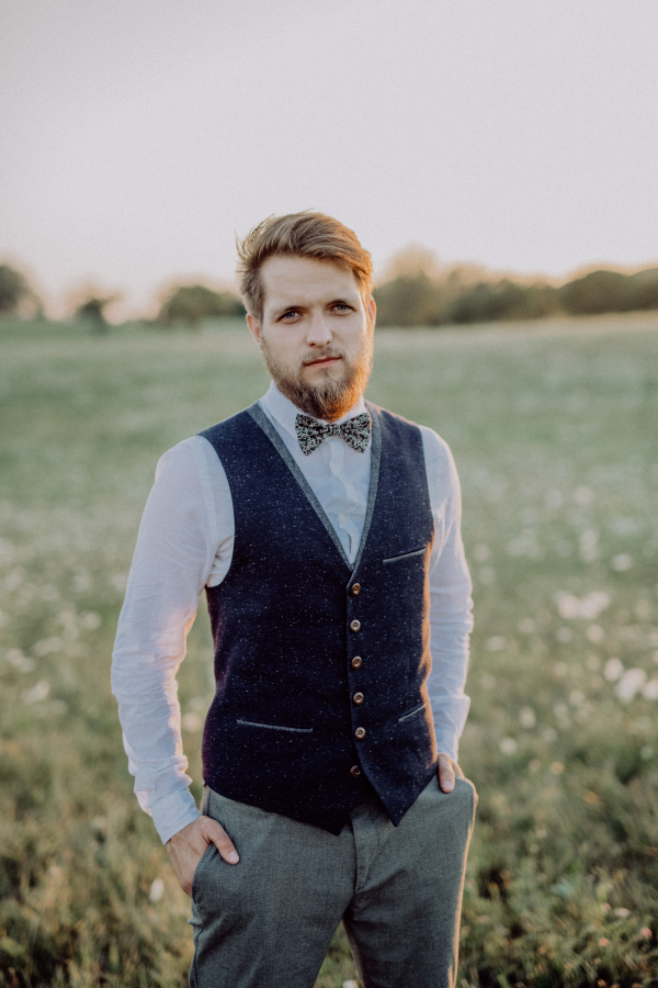 Handsome young groom posing outside in nature, hands in his pockets.