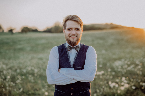 Handsome young groom posing outside in nature, arms crossed.