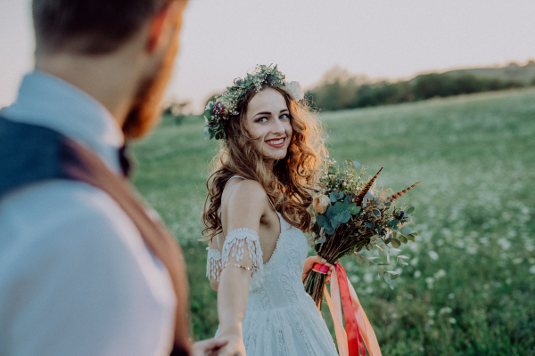 Beautiful young bride and groom outside in green nature at romantic sunset, holding hands.