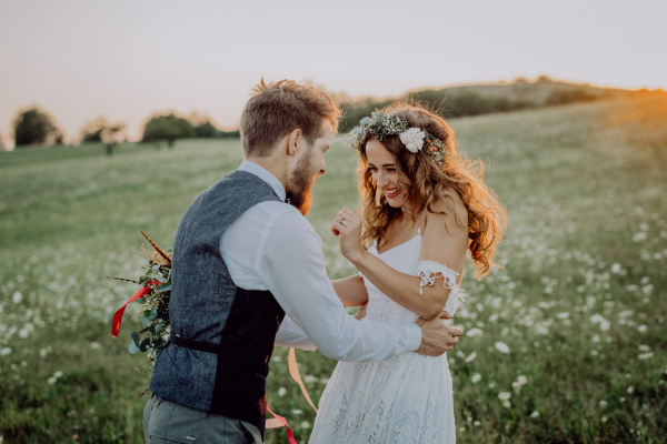 Beautiful young bride and groom outside in green nature at romantic sunset, having fun.