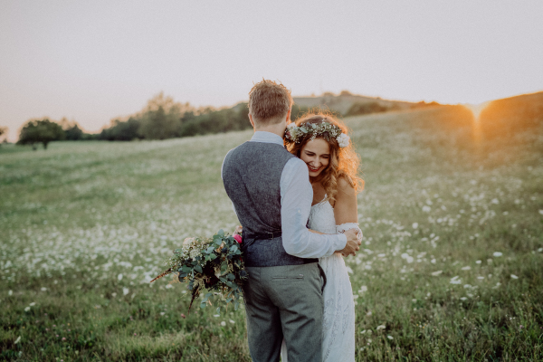 Young bride and groom outside in green nature at romantic sunset.