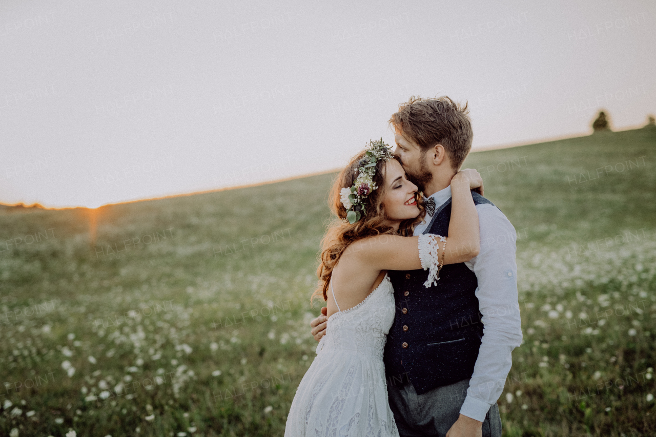 Young bride and groom outside in green nature at romantic sunset, hugging.