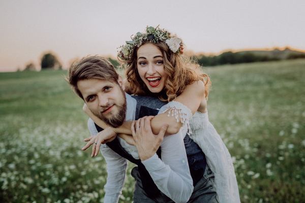 Beautiful young bride and groom outside in green nature at romantic sunset, having fun.