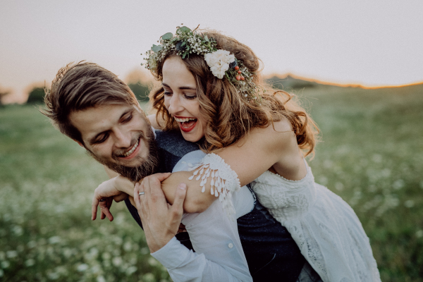 Beautiful young bride and groom outside in green nature at romantic sunset, having fun.