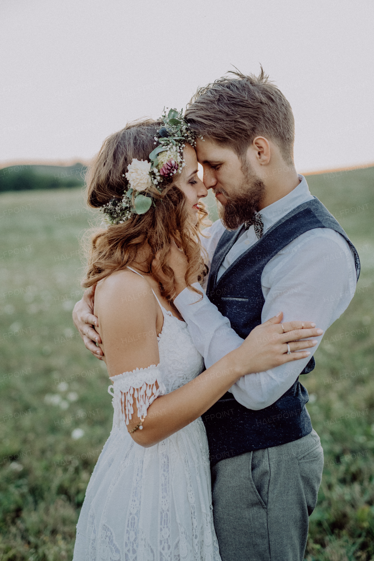 Young bride and groom outside in green nature at romantic sunset, hugging.