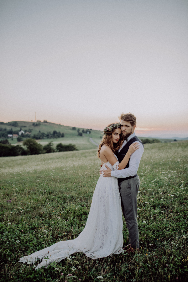 Beautiful young bride and groom outside in green nature at romantic sunset.