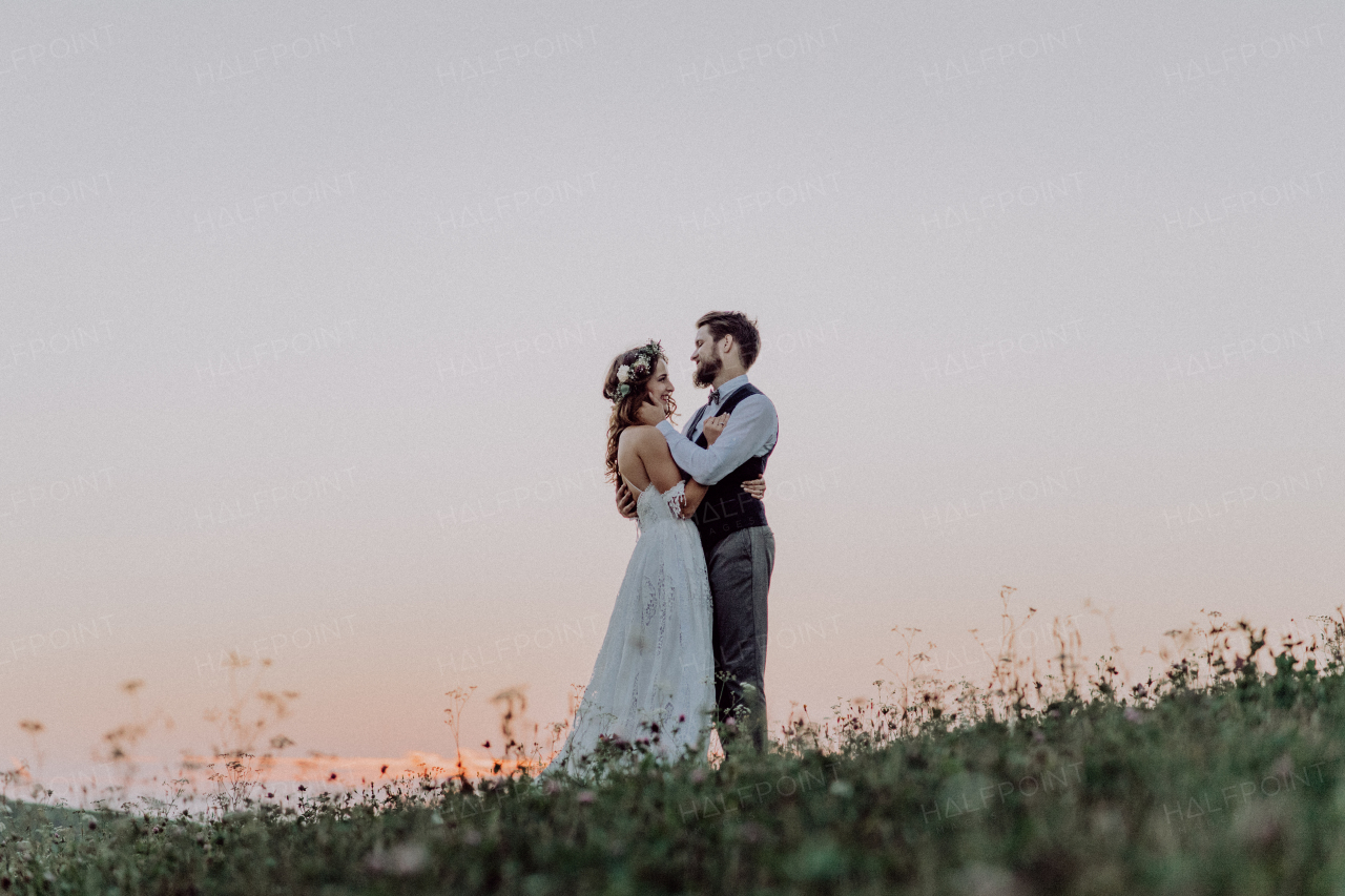 Young bride and groom outside in green nature at romantic sunset, hugging.