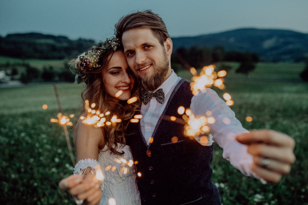 Beautiful young bride and groom in the evening on a meadow surrounded by chain of lights.