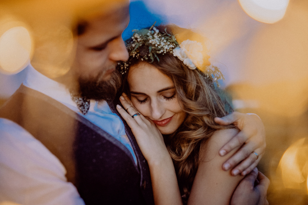 Beautiful young bride and groom at night on a meadow surrounded by chain of lights, hugging.