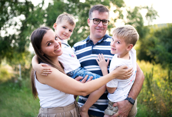 A cheerful young family holding two small sons outdoors in nature on a summer day, standing.