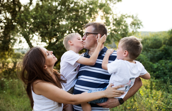 A cheerful young family holding two small sons outdoors in nature on a summer day, standing.