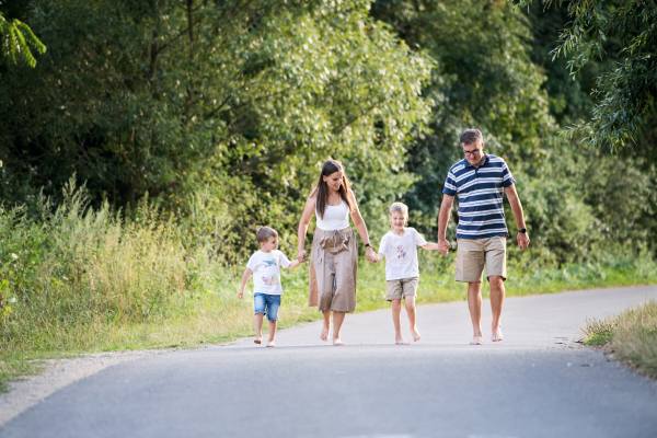 A young family with two small cheerful sons walking barefoot on a road in park on a summer day, holding hands.