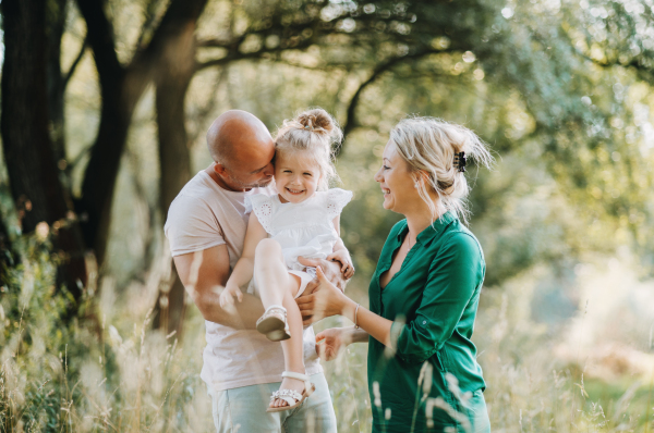 Young family with a small daughter spending time together in sunny summer nature.