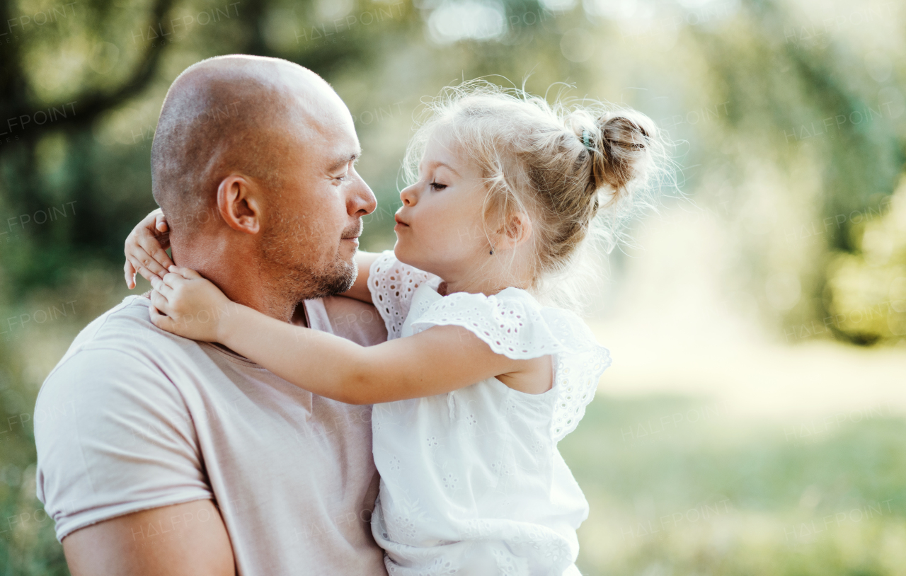 Handsome young father in green sunny summer nature holding his cute small daughter in the arms.