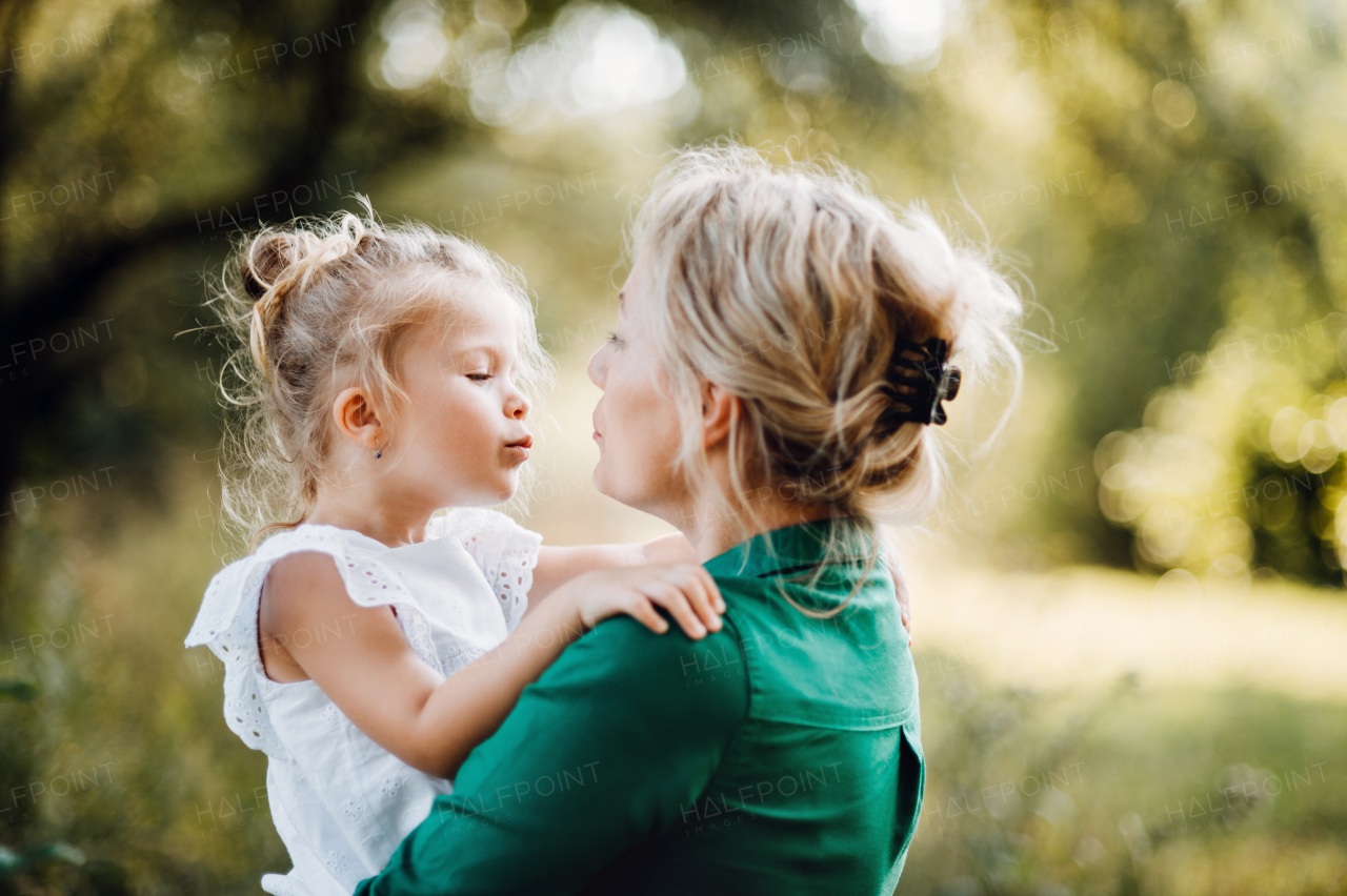 Beautiful young mother in green sunny summer nature holding her cute small daughter in the arms.