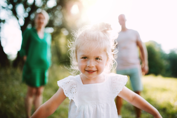 A small girl with unrecognizable parents in the background in sunny summer nature.