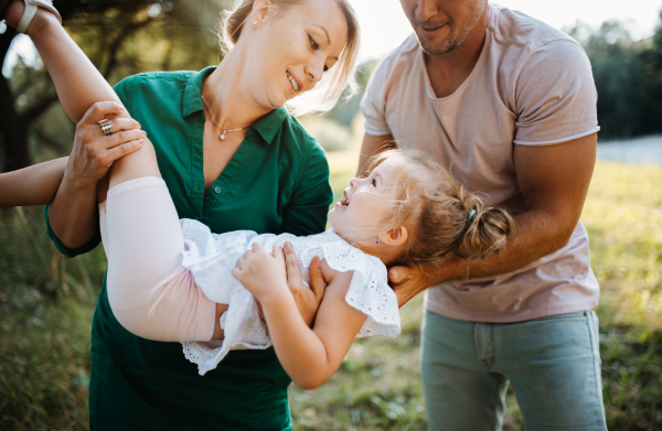 Young family with a small daughter spending time together in sunny summer nature, having fun.