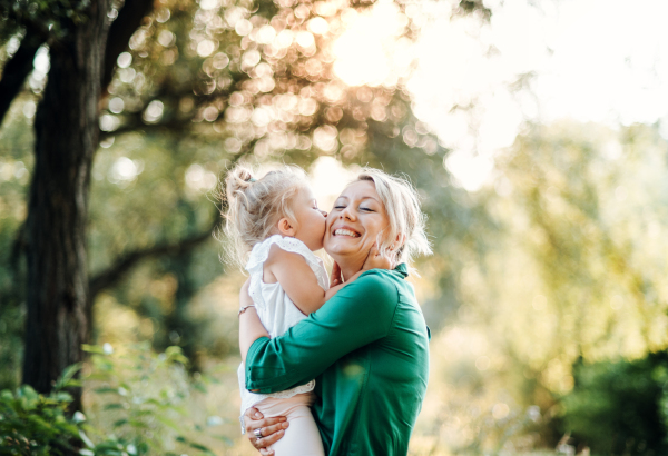 Young mother with small daughter on a meadow in nature, kissing.