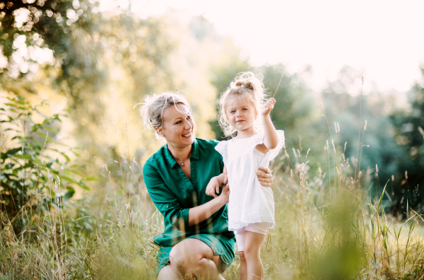 Beautiful young mother in green sunny summer nature holding her cute small daughter.