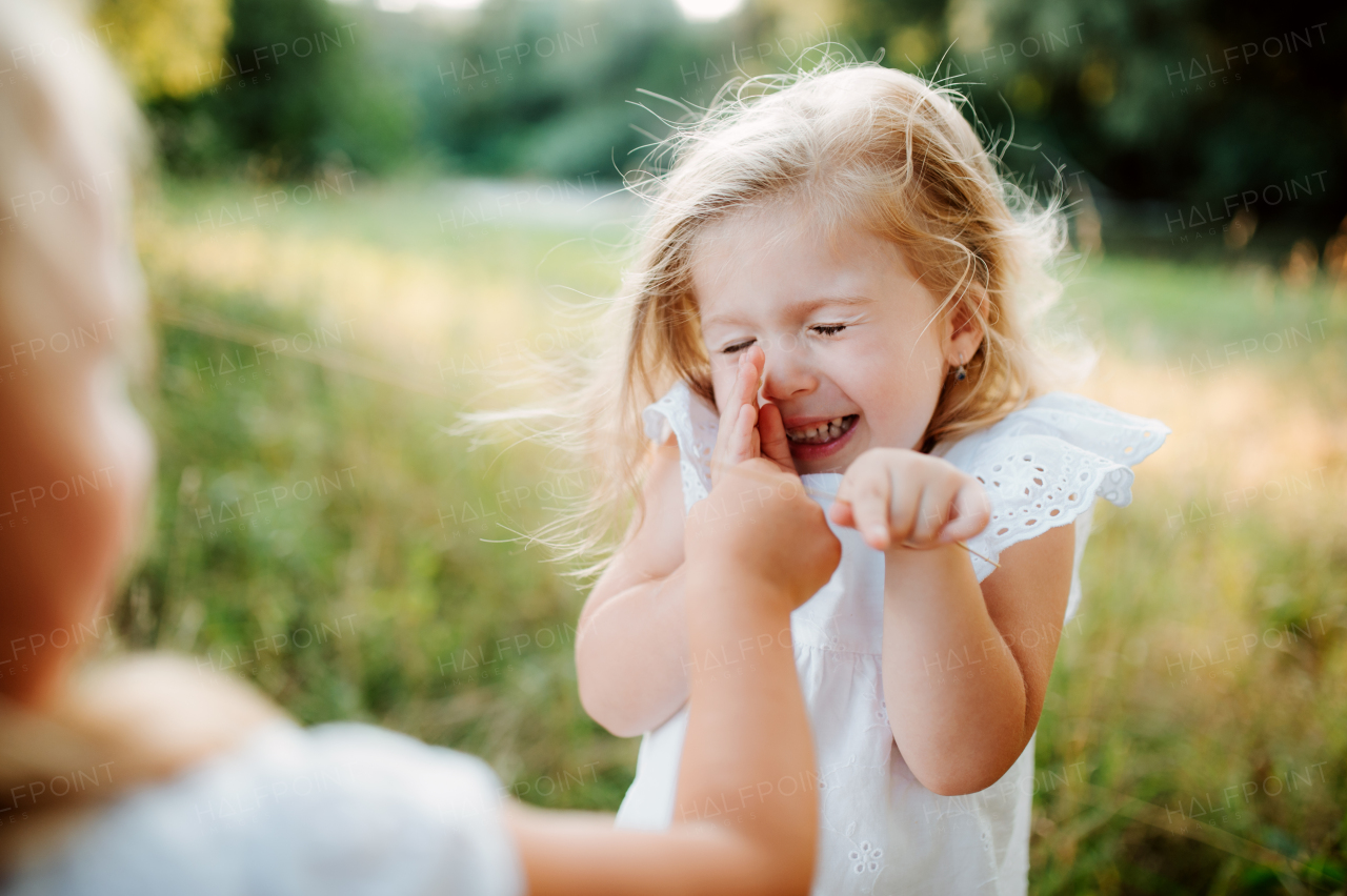 Two small girl friends or sister playing outdoors in sunny summer nature, having fun.