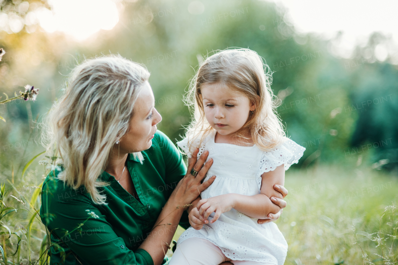 Beautiful young mother in green sunny summer nature holding her cute small daughter.