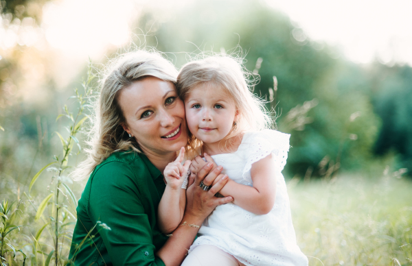 A portrait of young mother in nature with small daughter in summer. A front view.