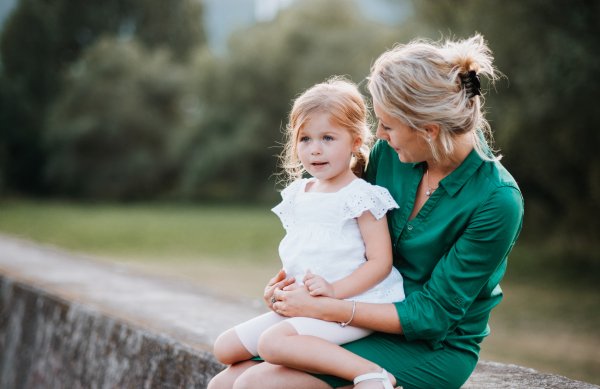 A young mother in nature with small daughter, sitting on stone wall.