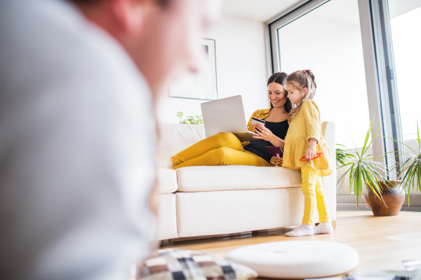 Young happy family with a child preparing for holiday at home. A woman using laptop and debit card, making online payment.