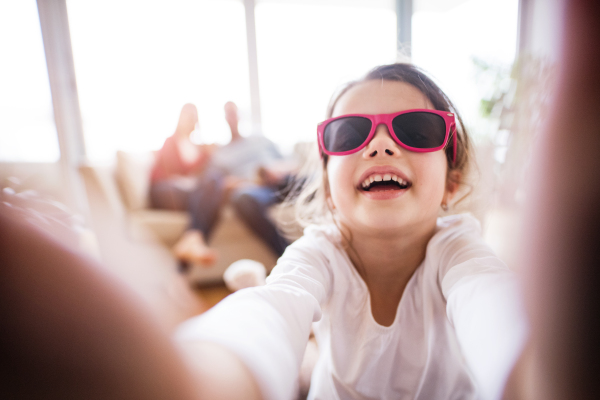 A cute small girl with unrecognizable parents taking selfie at home.