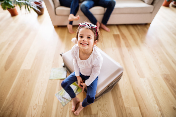 A small girl with unrecognizable parents packing for a holiday. A child sitting on a suitcase.