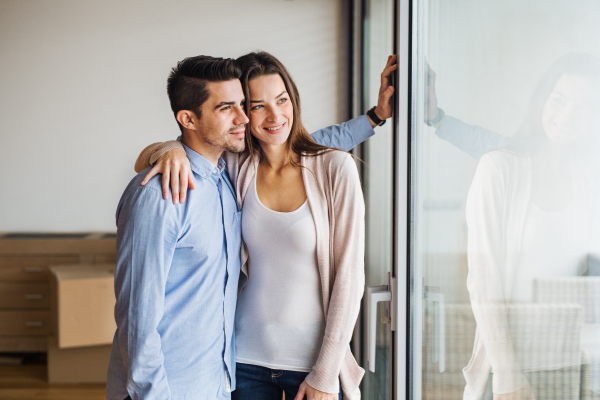 Young happy couple moving in a new home, standing by the window and looking out.