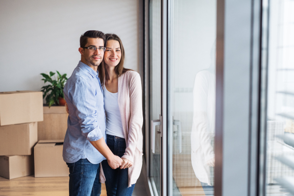 Young happy couple with cardboard boxes moving in a new home, hugging. Copy space.