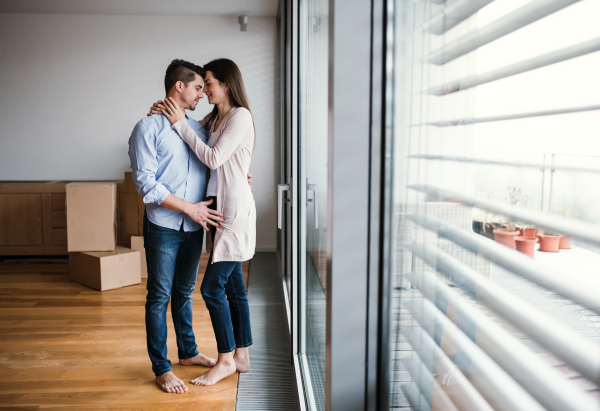 Young happy couple with cardboard boxes moving in a new home, hugging. Copy space.