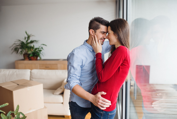 Young happy couple moving in a new home, standing by the window and hugging.