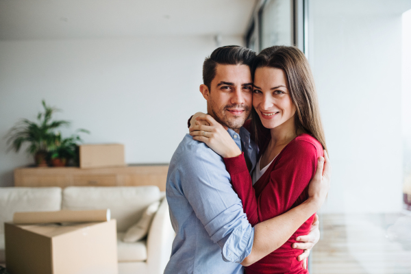 Young happy couple with cardboard boxes moving in a new home, hugging by a window.