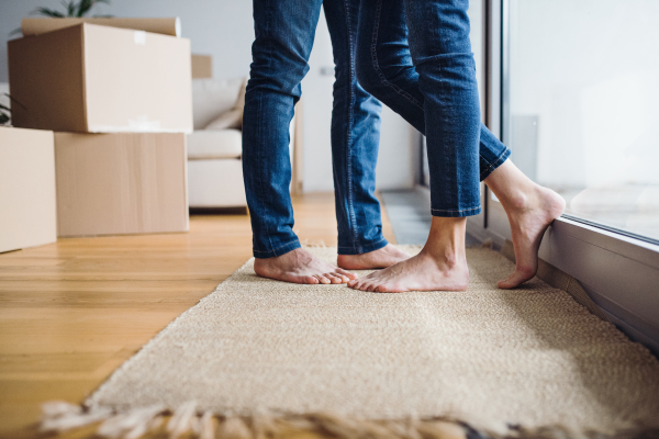 A midsection of legs and feet of young couple moving in a new home, standing by a window.