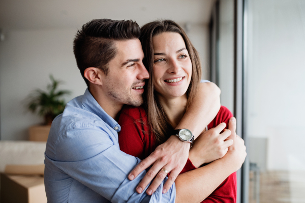 Young happy couple in love standing by the window at home, hugging.