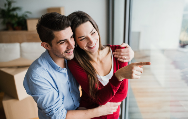 Young happy couple with cardboard boxes moving in a new home, looking out of a window.