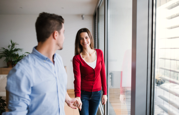 Young happy couple with cardboard boxes moving in a new home, holding hands.