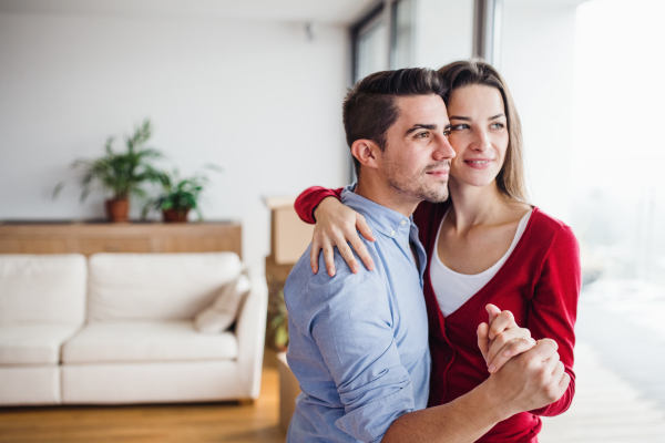 Young happy couple in love standing by the window at home, hugging. Copy space.