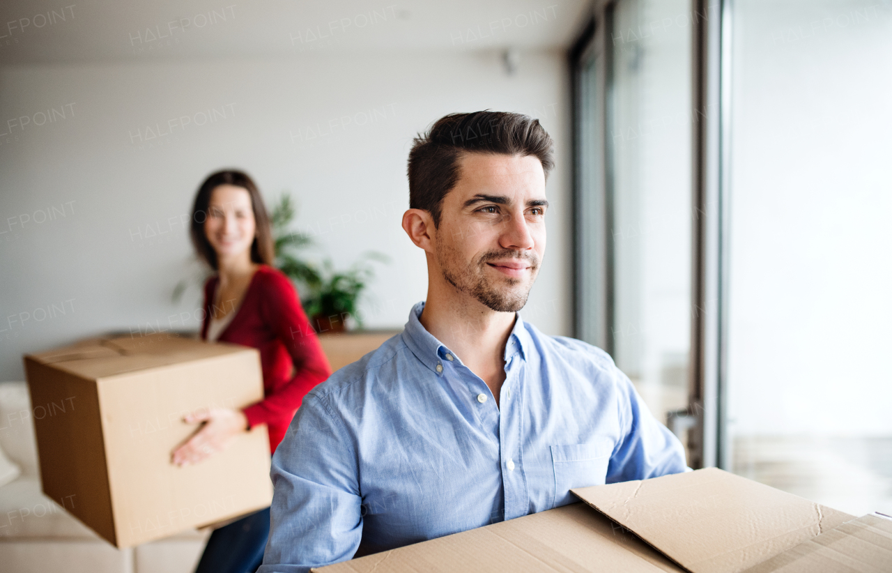 Young happy couple moving in a new home, holding cardboard boxes.