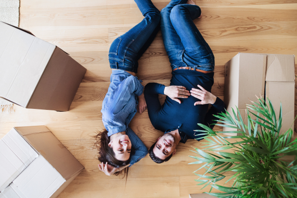 A top view of young happy couple with cardboard boxes lying on a floor, moving in a new home concept.