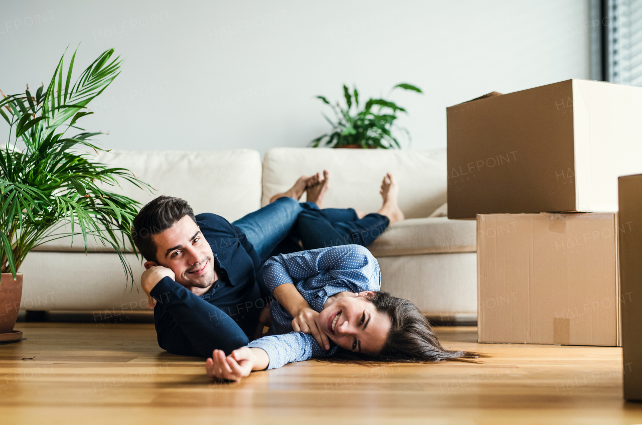 A young couple with cardboard boxes lying on the floor, moving in a new home.