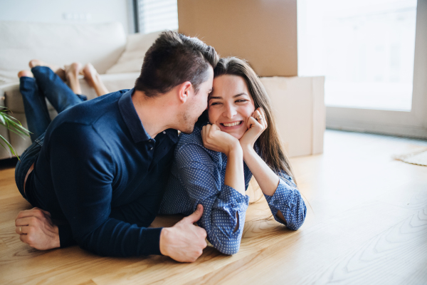 A young happy couple with a cup and cardboard boxes lying on a floor, moving in a new home.